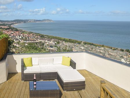A deck with a wicker sofa and table overlooking a town and the sea at Sea-Prize View in Old Colwyn