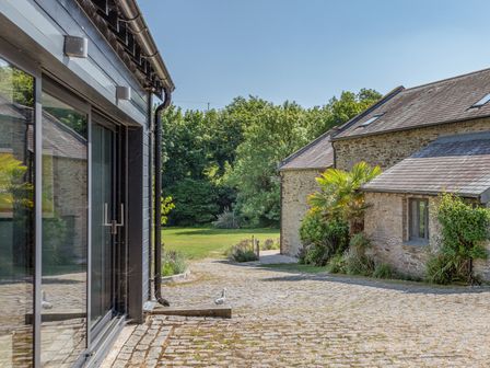 A cobblestone driveway with stone buildings and greenery at Linham Barn in Kingsbridge