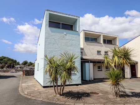 A white and light blue two-story building with several windows and palm trees outside on a paved sidewalk at 1 South Snowdon Wharf in Porthmadog