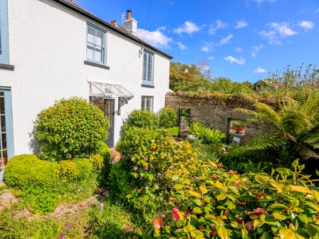 A garden with green shrubs and flowers in front of a white house with blue window frames at Rosevine in Slapton
