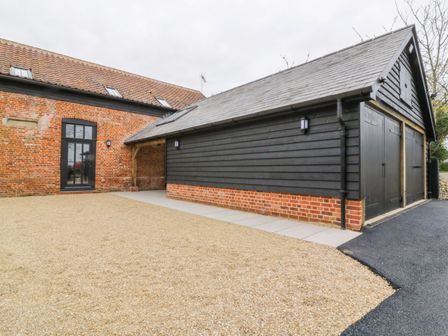 An exterior view of a building with black wooden cladding and brick base next to a building with red brick walls and tiled roof at Grange Barn in Gedding near Felsham