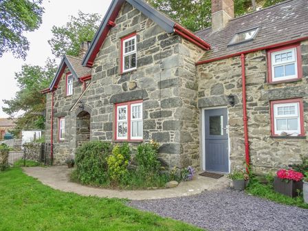 A stone house with red window frames and a grey door surrounded by grass and plants at Hafodty in Conwy