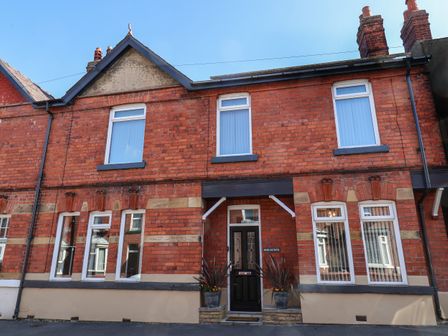 A red brick two-story house with multiple white-framed windows and a black door with two plants on either side at Moorland House in Scarborough