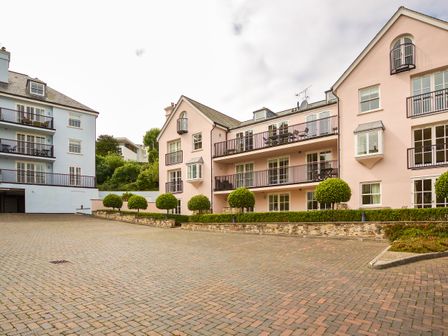 A paved parking area in front of apartment buildings with balconies and trimmed trees at 14 Combehaven in Salcombe