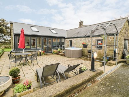 An outdoor patio with lounge chairs a table with chairs and an umbrella a hot tub and stone walls at Meadowside in Mousehole