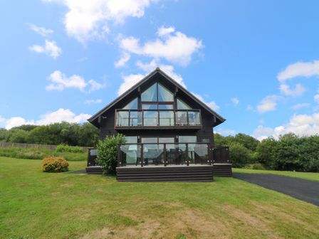 A two-story wooden lodge with glass balconies on a grassy lawn at Willow Retallack in Retallack near St Columb Major