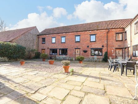 A courtyard with potted plants tables and chairs in front of a brick building at The Dairy Barn in Toftrees near Fakenham