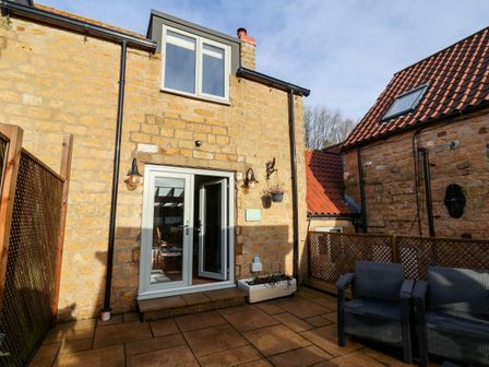 A stone house exterior with a patio area and outdoor seating at Tawny Cottage in Irton Moor near Scarborough
