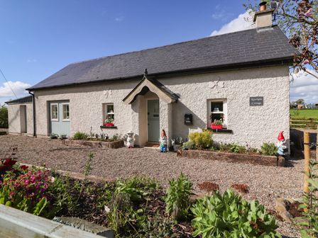 A single story cottage with a pitched roof garden gnomes and flowers in front at Lynchpin Cottage Carrigeen near Bruff