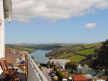 A balcony with wooden chairs and a table overlooking a river and green hills at 3 Melbury in Salcombe