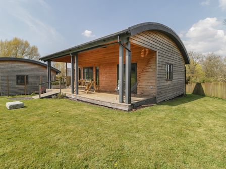 A wooden cabin with a covered porch and outdoor seating on a grassy lawn at Foxglove in Sticklinch West Pennard Glastonbury