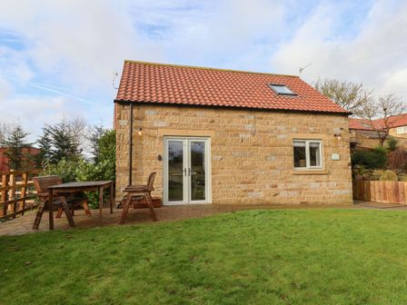 A stone house with a red tiled roof a grassy yard and wooden picnic table with benches outside at The Stables in Seamer North Yorkshire