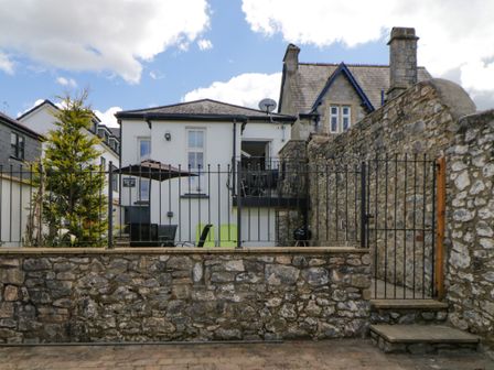 Backyard patio with table umbrella chairs stone wall and black metal gate at Old Anvil Cottage in Chudleigh