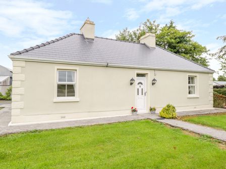 The exterior of a single story house with two windows a white door two wall lamps and a lawn at Cherry Tree Cottage in Ballintober near Castlebar County Mayo
