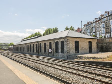 A railway platform with train tracks and a long stone building with arched windows at Blue Peter @ Engine Shed in Whitby