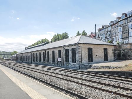 A railway platform with multiple train tracks alongside a long stone building and residential buildings in the background at Olton Hall @ Engine Shed in Whitby