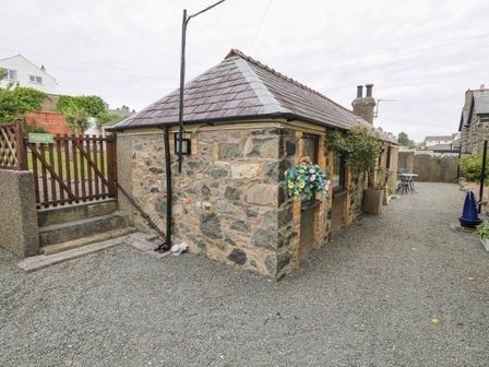 A stone cottage with a slate roof and a gravel yard with outdoor furniture and hanging flowers at Fir Tree Cottage in Criccieth