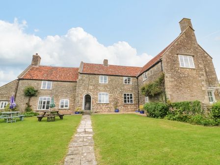 A stone farmhouse with a tiled roof and green lawn with picnic tables and umbrellas at Butcombe Farm House in Butcombe