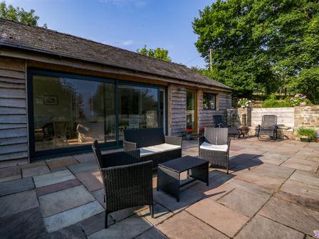 An outdoor patio with black wicker furniture and stone flooring adjacent to a wooden building at Black Cat Bach in Gilwern