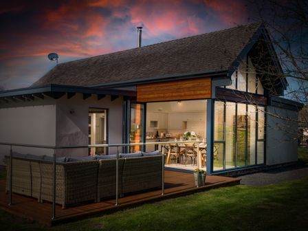 A house with an outdoor seating area and a kitchen visible through large glass doors at Lambs Lodge in Bamburgh