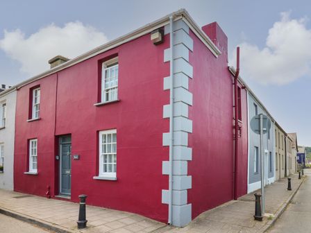 A red corner house with white trimmed windows and a blue door at Bari in Aberaeron