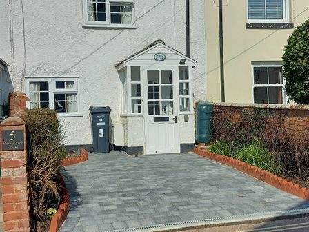 Exterior front view of a house with a paved driveway and a white door at Meadow View Cottage in Lympstone