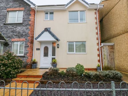 The front exterior of a two-story house with a white door a small porch garden plants and a fence at Ty Cerrig in Cwmgors