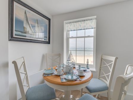 A small dining area with a round table set for four near a window with a view of the beach and ocean at 5 The Beaches Weymouth
