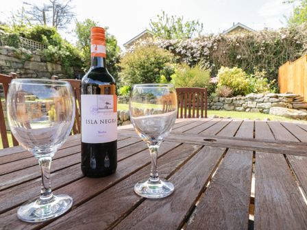 A bottle of Isla Negra wine and two empty wine glasses on a wooden table in a garden with chairs and stone walls at Clyd Fan in Harlech