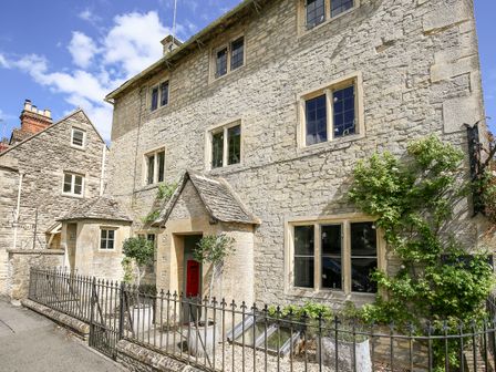 A stone house with multiple windows a doorway with a small porch two potted plants and a red mailbox at The Old Post Office in Coln St Aldwyns
