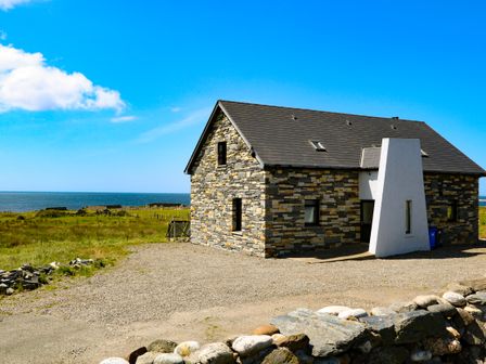 A stone house with a sloped roof near a grassy field and the sea at Ocean Sail House in Termon near Dungloe County Donegal
