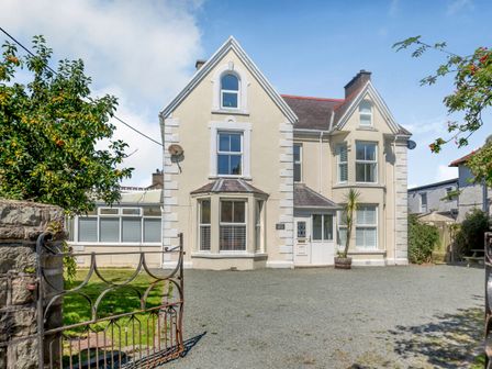 A large cream colored house with multiple windows and a gravel driveway at Bryn Rhosyn in Nefyn