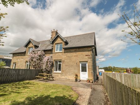 An exterior view of a stone house with a fenced garden and a wooden picnic table at Appletree in Alnwick
