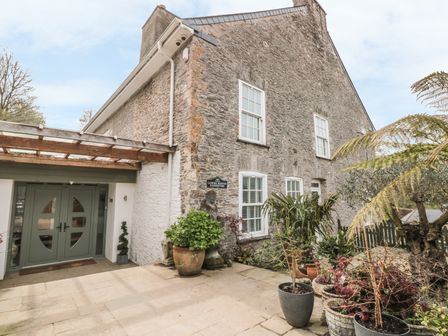 An exterior view of a stone building with green double doors and several potted plants at Lower Norton Farmhouse in Dartmouth