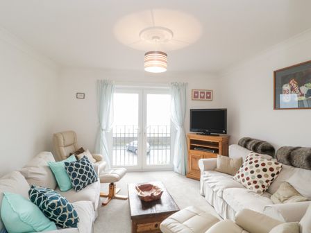 A living room with sofas cushions a wooden coffee table armchairs a television on a cabinet and glass doors at 14 Lyme Mews in Seaton Devon