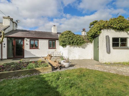 A garden area with a cottage, table, and chairs at Bwthyn in Moelfre