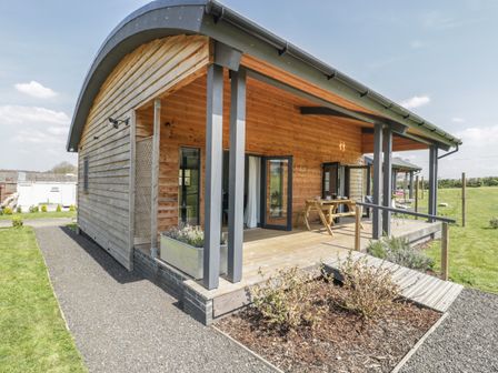 A wooden cabin with a covered porch and picnic table in a grassy area at Primrose Sticklinch West Pennard Glastonbury