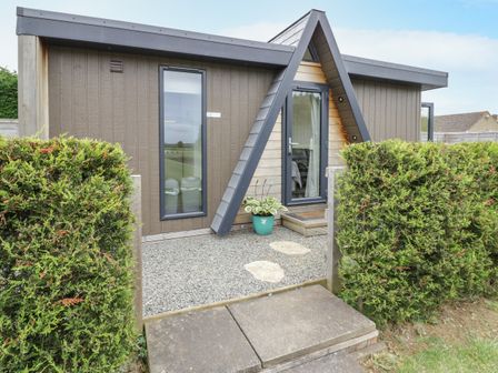 A modern cabin with a triangular entrance door two tall windows and hedges on either side at Alstroemeria Bretforton near Evesham