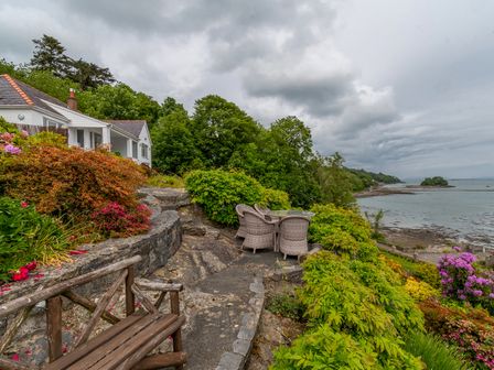 A garden with chairs and a table overlooking a coastline at Swn Y Wylan in Menai Bridge