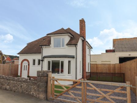 A two-story house with a brown tiled roof white walls and a brick chimney behind a stone wall and wooden gate at Greystones in Llandudno