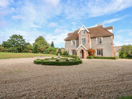 A large stone house with a circular hedge and fountain in front in a gravel driveway at Southrepps Lodge in Southrepps