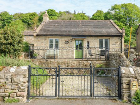 A stone cottage with a green door and windows behind a black metal gate at Sunshine Cottage in Preston under Scar near Leyburn
