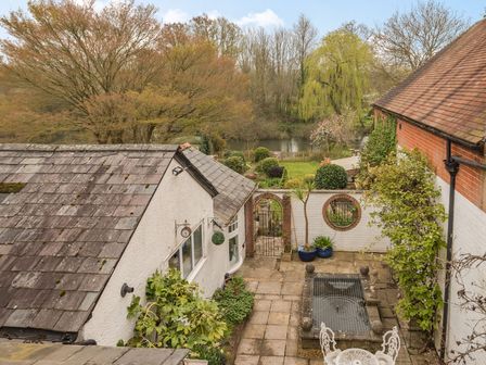A garden with a pond and patio area between two buildings at Riverside House in Fordingbridge