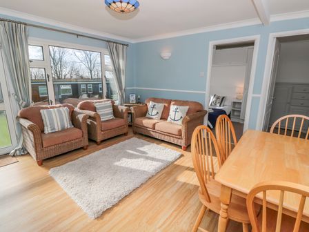 A living room with wicker sofas, a wooden dining table with chairs, a white rug, and a large window at The Borrowers in Dartmouth