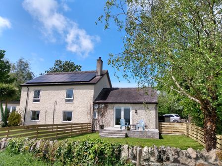 A two-story house with solar panels on the roof and a fenced garden with outdoor chairs at Plas Marchog Annexe in Rhoscefnhir near Pentraeth