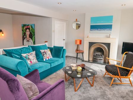 A living room with a turquoise sofa purple armchair black patterned chair glass coffee table and fireplace at 34b Clarence Street in Dartmouth