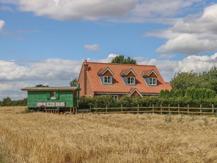 A red brick house with orange tiled roof next to a green wooden structure in a field of golden crops at Wayside Cottage in Pocklington
