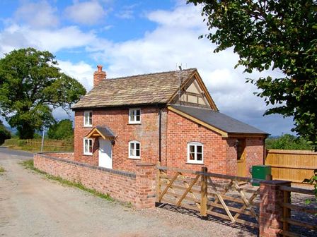 A brick cottage with a wooden gate and stone roof along a country road at Point Cottage in Preston-on-Wye near Hereford