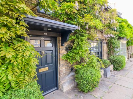 The entrance to a stone cottage with a dark blue door surrounded by green vines and plants at Murton Cottage in Burford