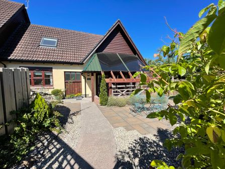 A house with a tiled roof and front garden with patio furniture at The Forge in Shipham